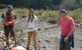 Three people introducing water sampling methods along a river